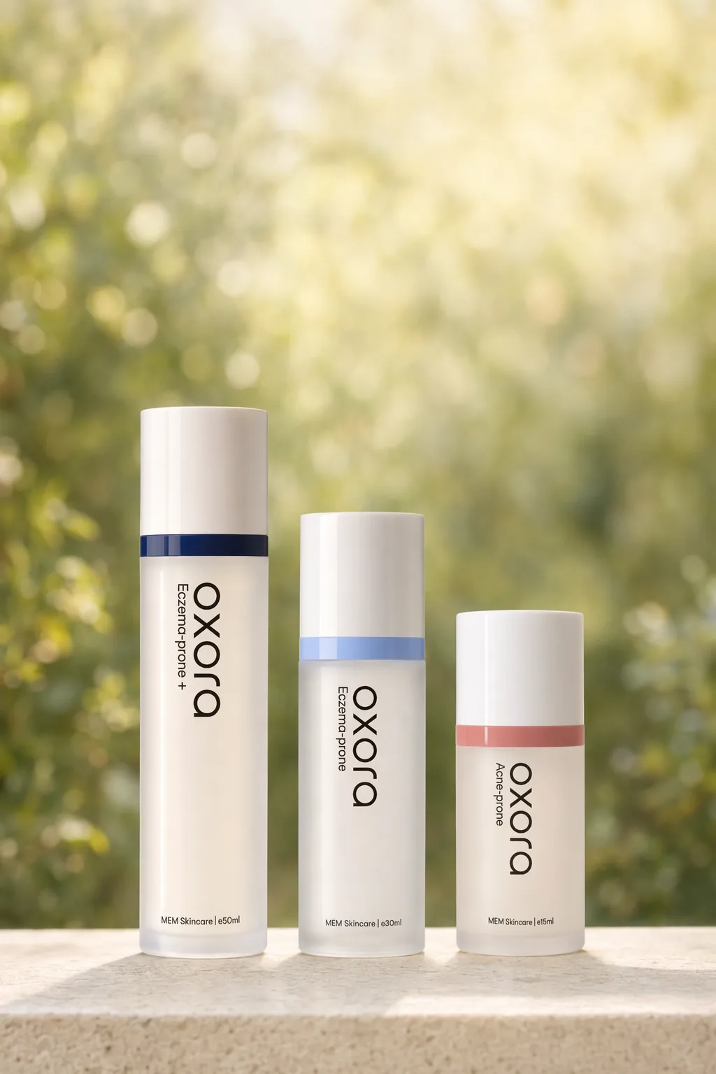 Oxora Acne-prone, Eczema-prone and Eczema-prone Plus Skin Base Fluid in 15 ml, 30 ml and 50 ml airless pump bottles, on a sunlit ledge